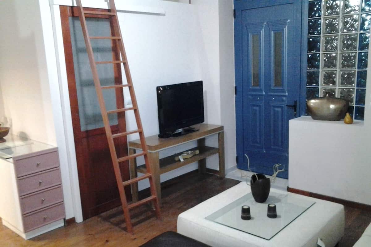 A compact living space with a television on a wooden stand, a blue door, and a white cabinet with drawers.