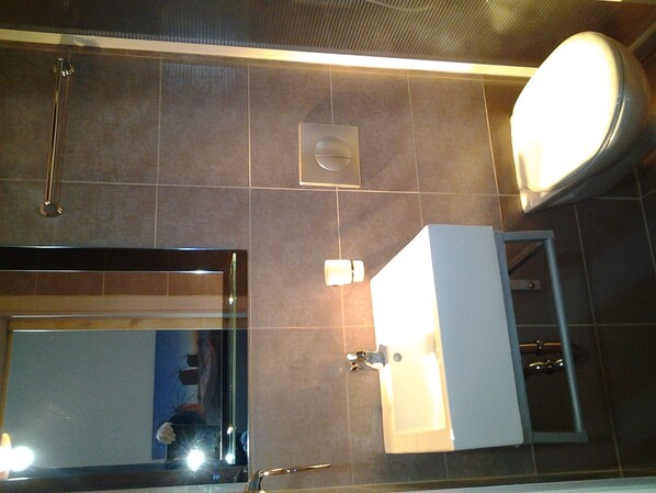 A bathroom with a large mirror, a toilet, a sink, and a shower.