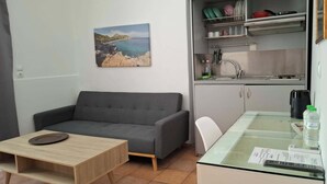 A compact living space with a sofa, a dining table, a kitchen area, and a view of the sea. - Mastic Point Studios (Chios)