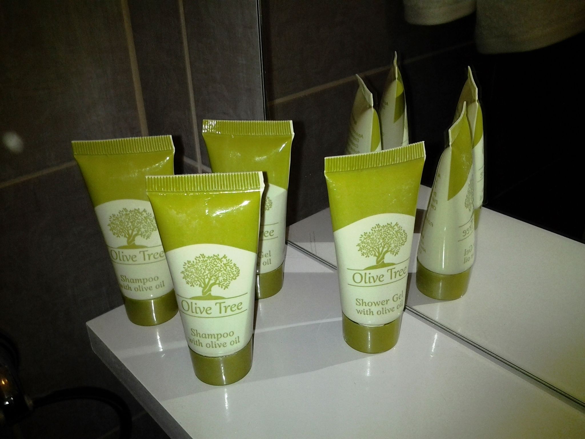 Un baño con un lavabo blanco y varias botellas de champú y gel de ducha Olive Tree.