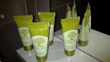 Un baño con un lavabo blanco y varias botellas de champú y gel de ducha Olive Tree.