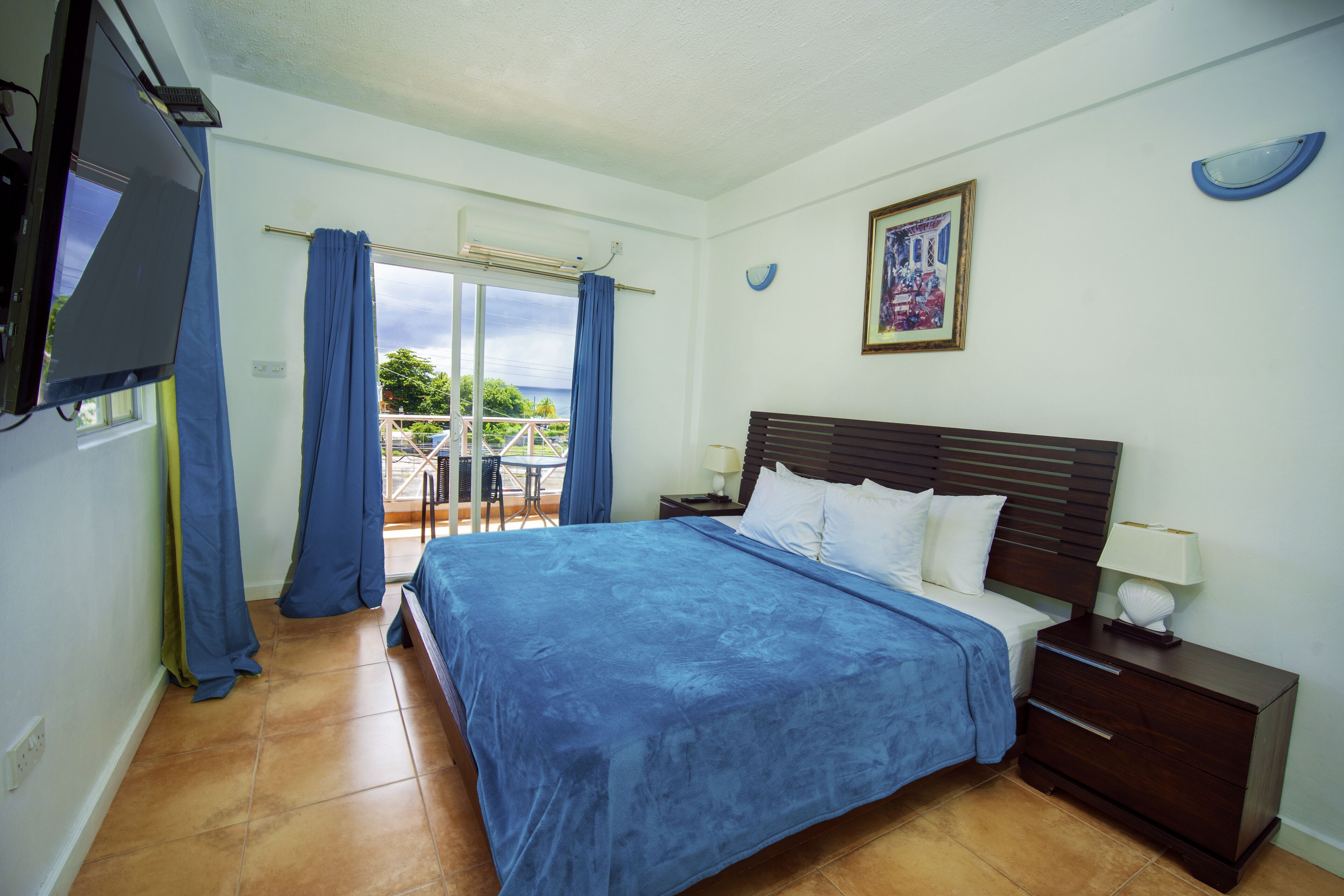Quarto com cama, mesa de cabeceira, televisão e vista para o exterior.