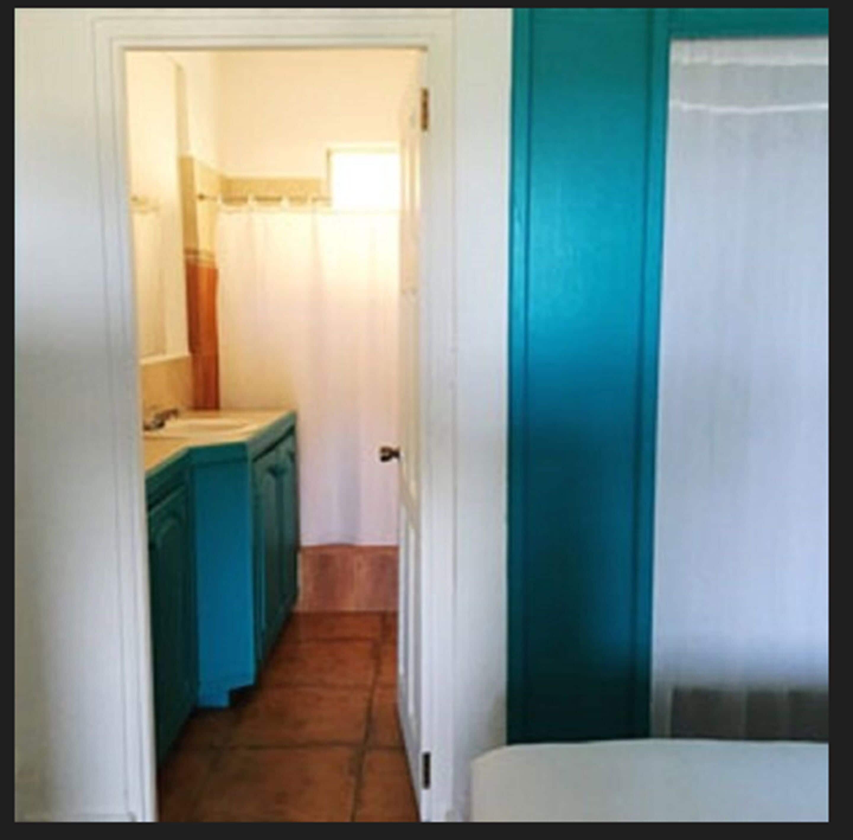 A narrow hallway with a bathroom on the left and a door on the right.