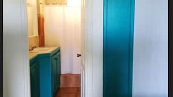A narrow hallway with a bathroom on the left and a door on the right.