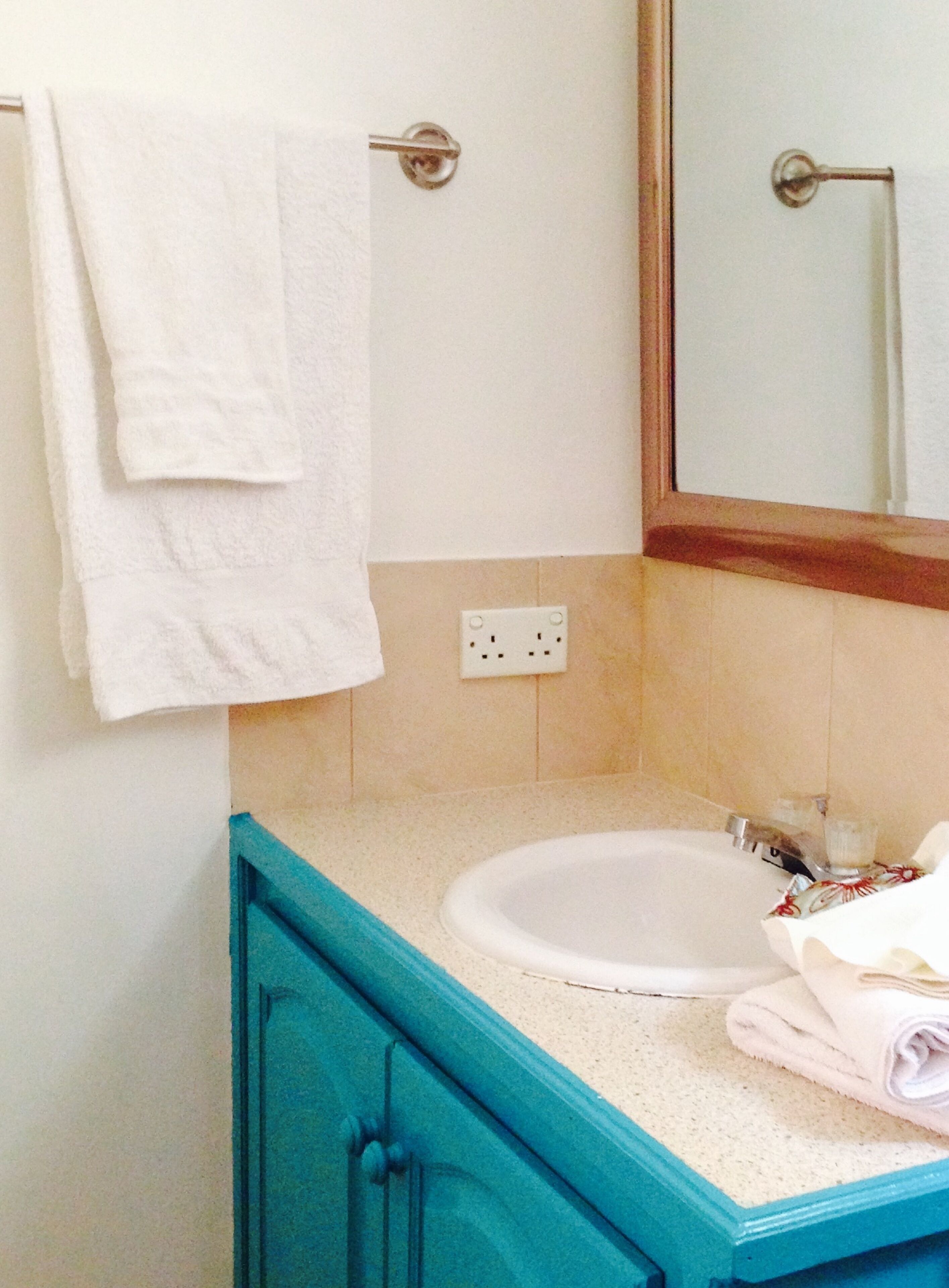 Un baño con un lavamanos blanco, un espejo y una toalla colgada en un perchero.
