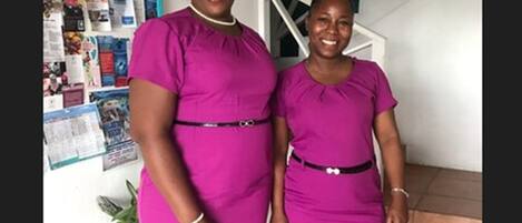 Two individuals standing indoors, one wearing a pink dress and the other in a darker shade.