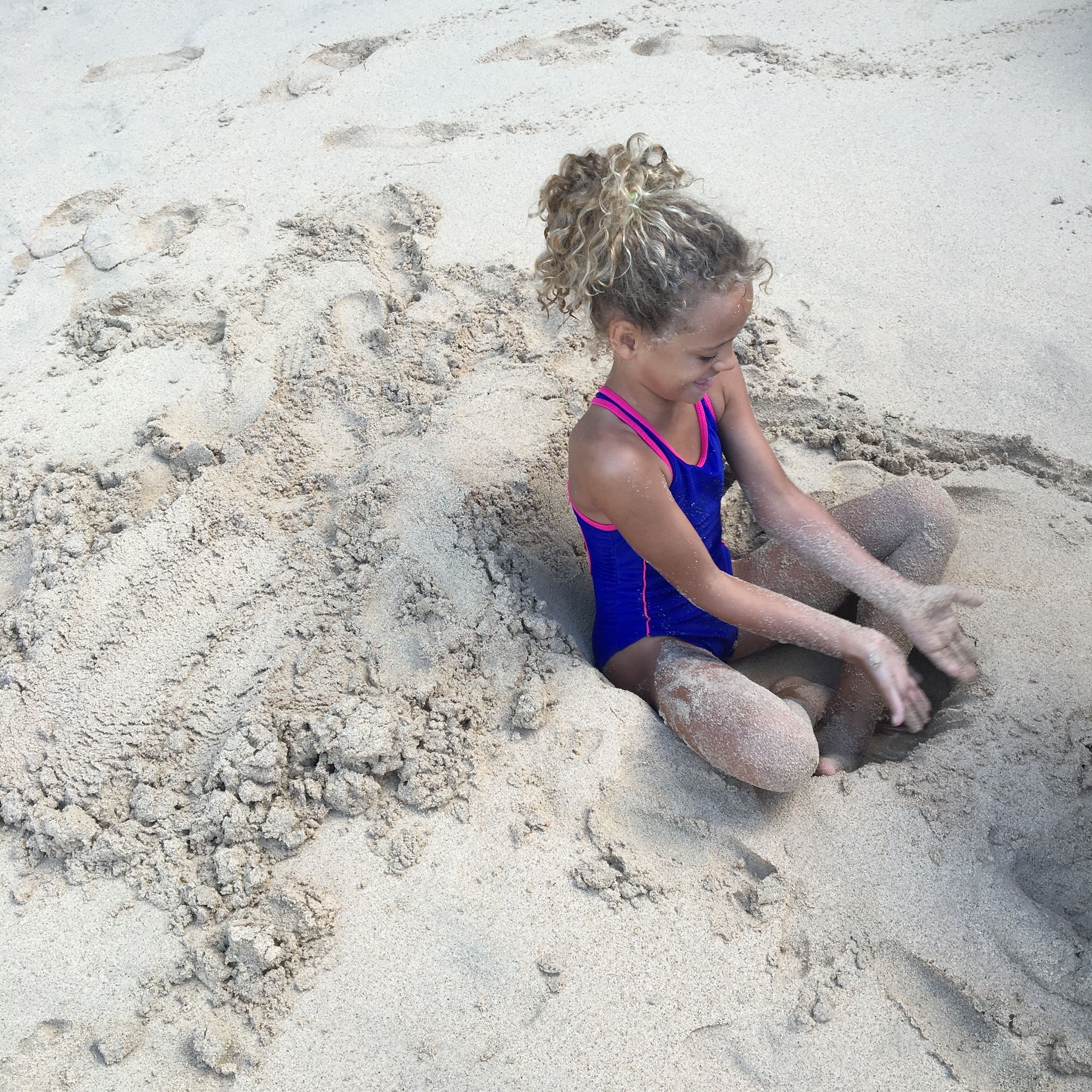 En person sidder i et sandet område, måske en strand eller sandkasse.