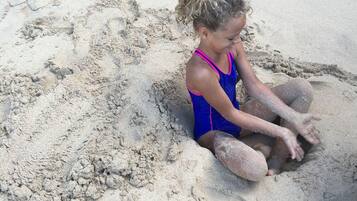 Una persona sentada en una zona arenosa, posiblemente una playa o un arenero.