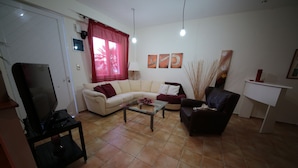 A living room with a sofa, a coffee table, a TV, and a small table with a lamp. - Point Twins Apartments (Chios)