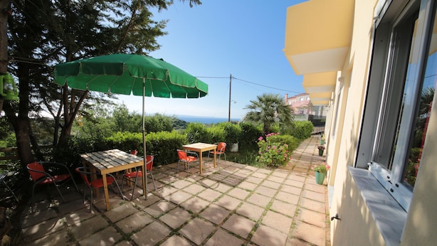 A patio with a table and chairs, a green umbrella, and a view of the sea. - Point Twins Apartments (Chios)