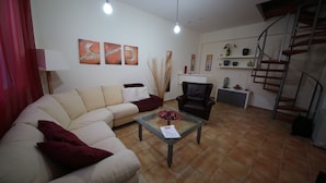 A living room with a sofa, a glass coffee table, a chair, and a spiral staircase. - Point Twins Apartments (Chios)