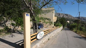 A road with a wooden fence, a sign reading "18", and a car parked on the side. - Point Twins Apartments (Chios)