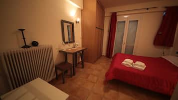 A hotel room with a bed, a desk, a chair, a radiator, a mirror, and a window with curtains.
