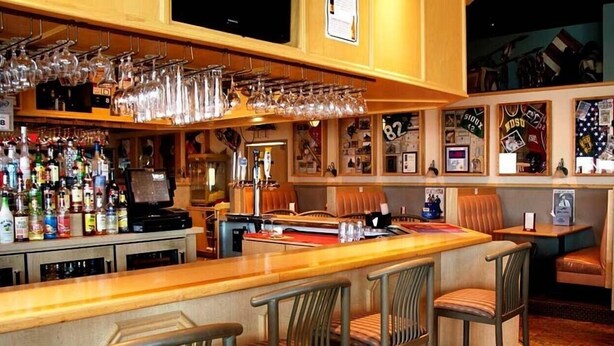 Zona de bar con mostrador de madera, varios taburetes y una variedad de botellas de licor.