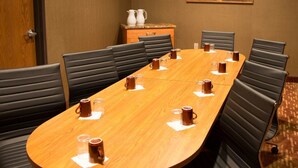 Un salón de conferencias con una larga mesa de madera, sillas de cuero negro y un cuadro en la pared.