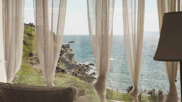 A room with a view of the sea through sheer curtains, a lamp, and a bed. - Poseidon Beach Villas (Lavreotiki)