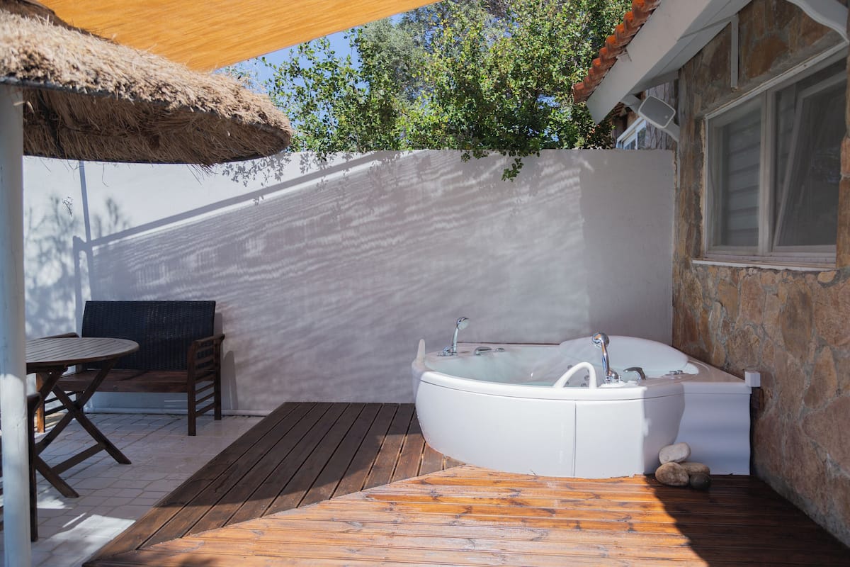 A spa area with a hot tub, wooden deck, and a thatched umbrella.