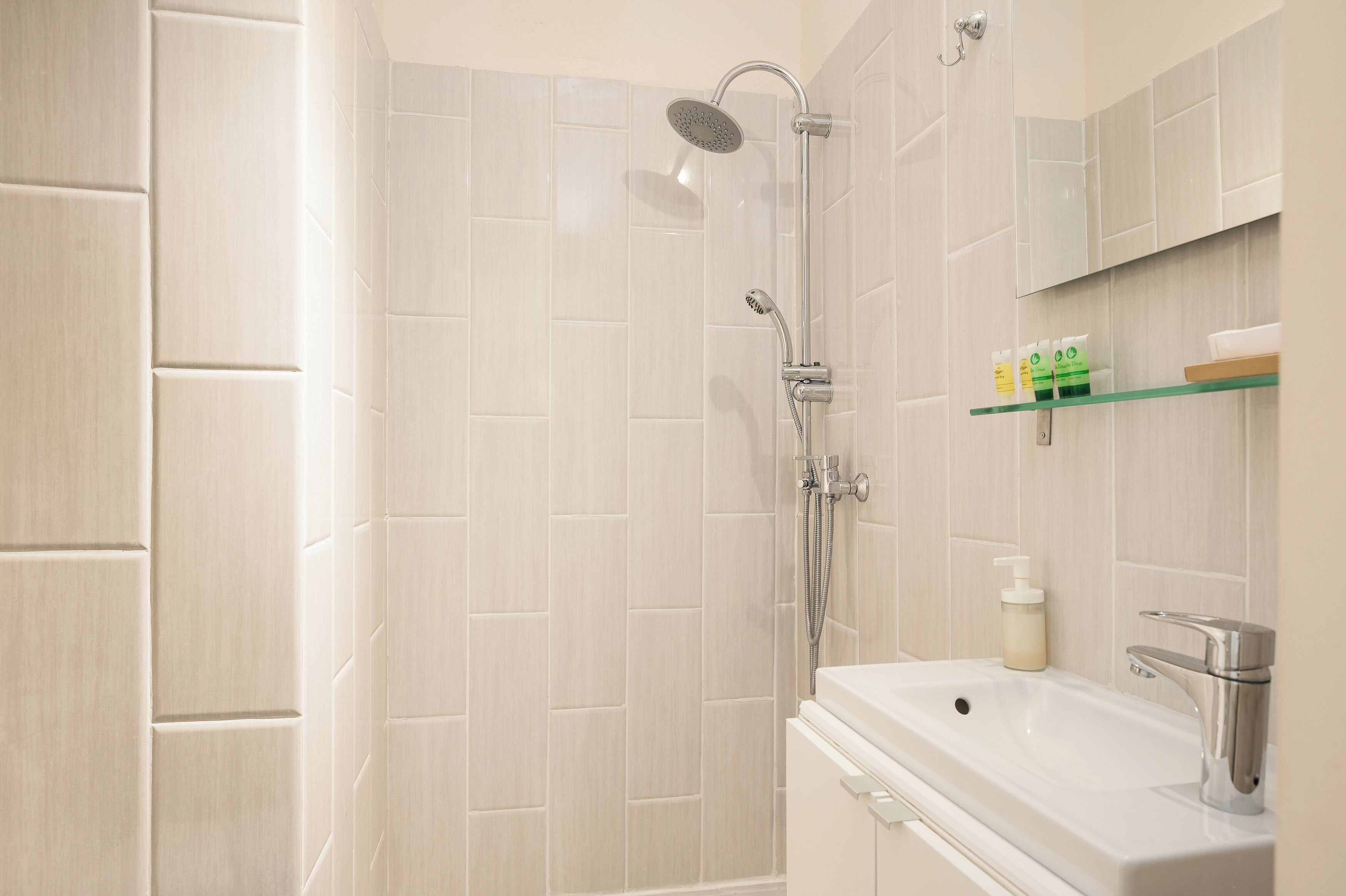 A bathroom with a shower, sink, and toiletries on a shelf.