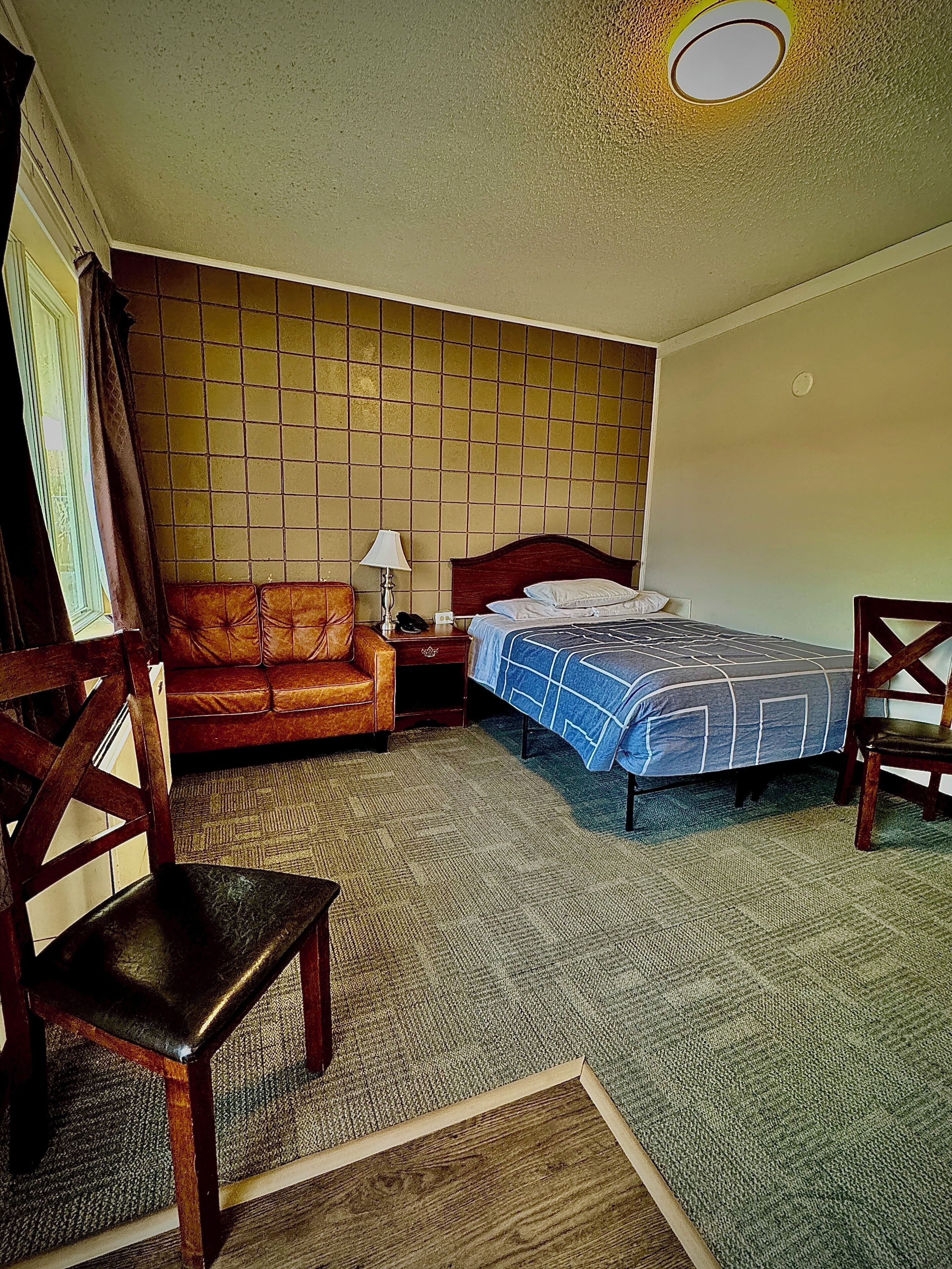 A hotel room with a bed, a sofa, a chair, a nightstand, and a lamp.