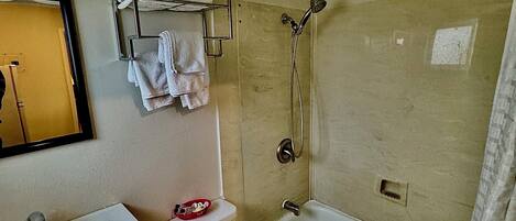 Un baño con lavamanos, inodoro y bañera. Hay un perchero con toallas y un cabezal de ducha.