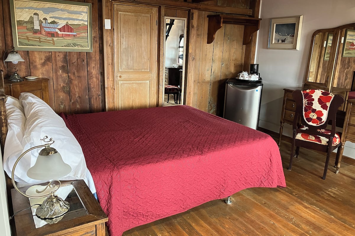 Une pièce en bois contenant un lit, une chaise, une table de chevet, une lampe et un réfrigérateur.