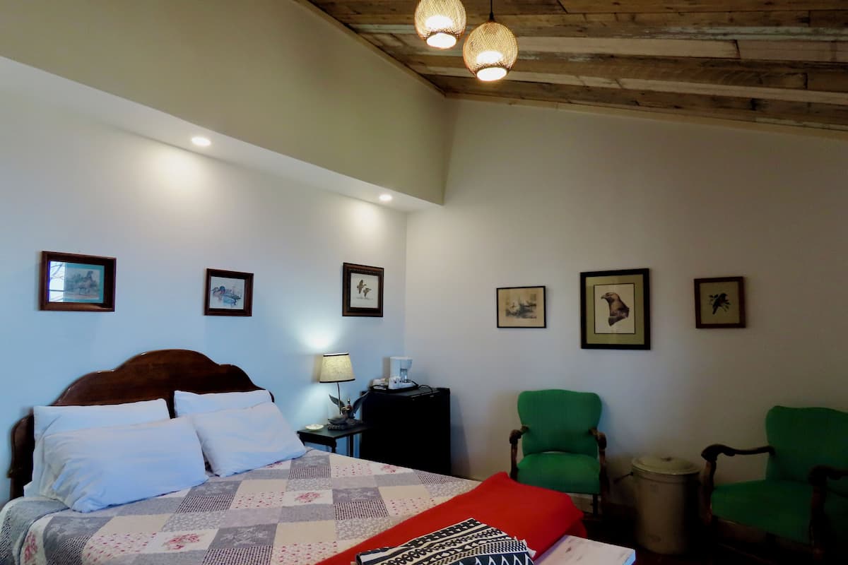 Une chambre à coucher avec un lit, une table de chevet, une lampe, une chaise et des tableaux encadrés au mur.