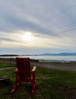 Uma cadeira Adirondack vermelha virada para um corpo d'água, com montanhas ao fundo.