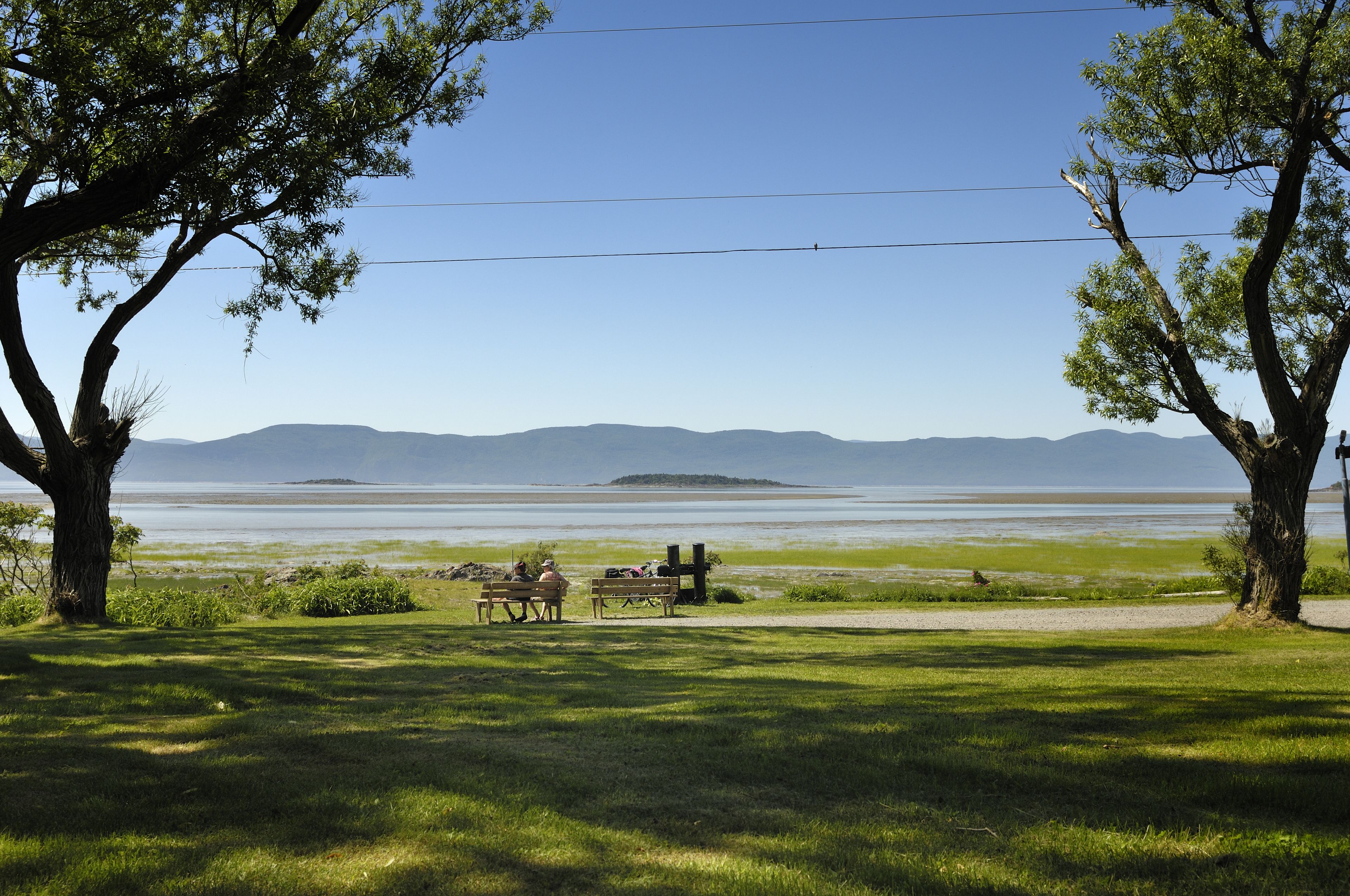 A grassy area with two benches and a picnic table, overlooking a body of water and distant hills.