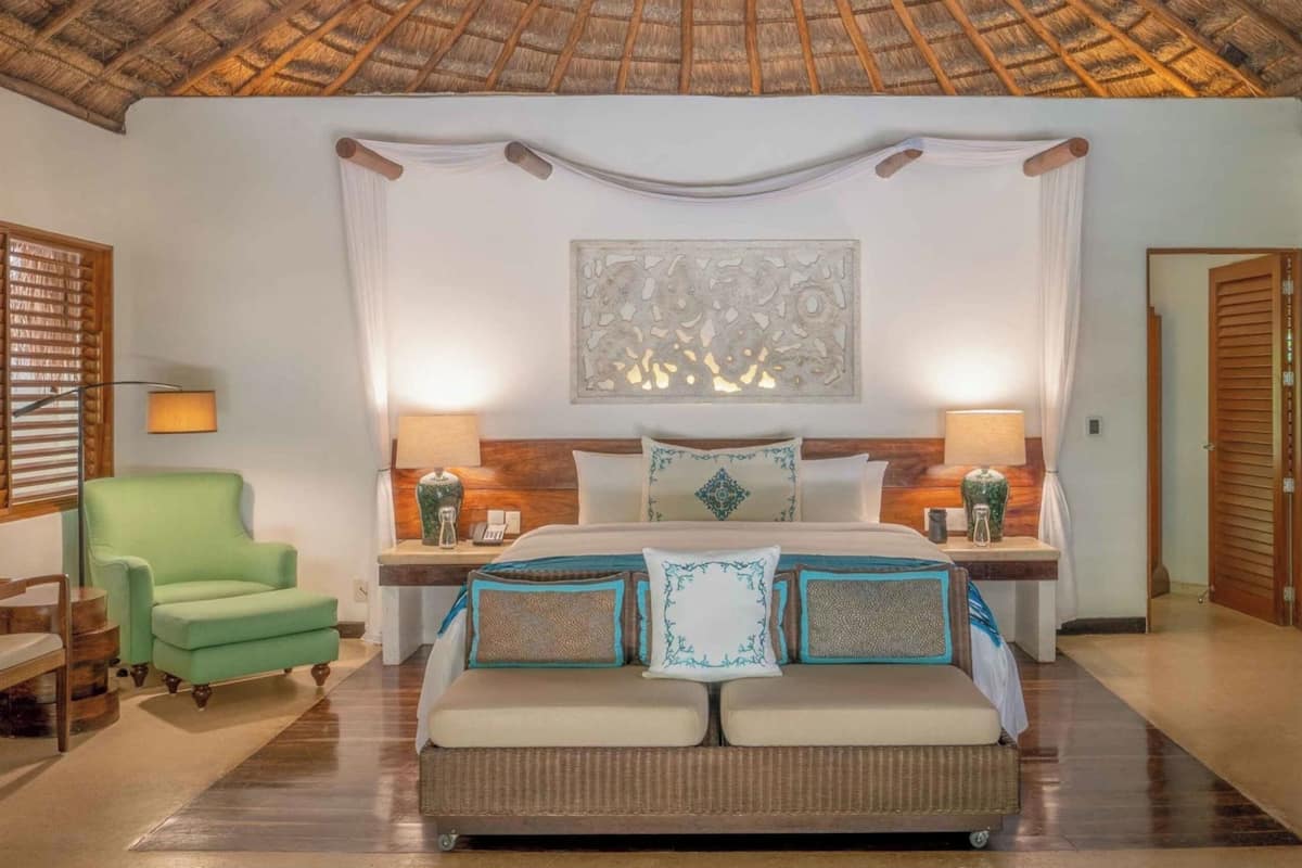 Une chambre d’hôtel avec un lit, deux tables de chevet, un fauteuil vert et un élément décoratif mural.