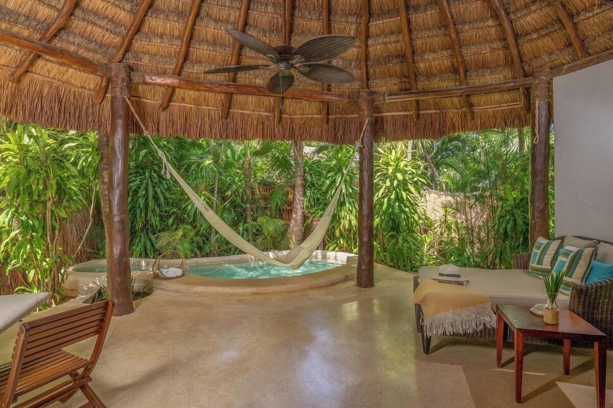 Un espace extérieur doté d’un toit de chaume, d’un hamac, d’une piscine et de mobilier d’extérieur.