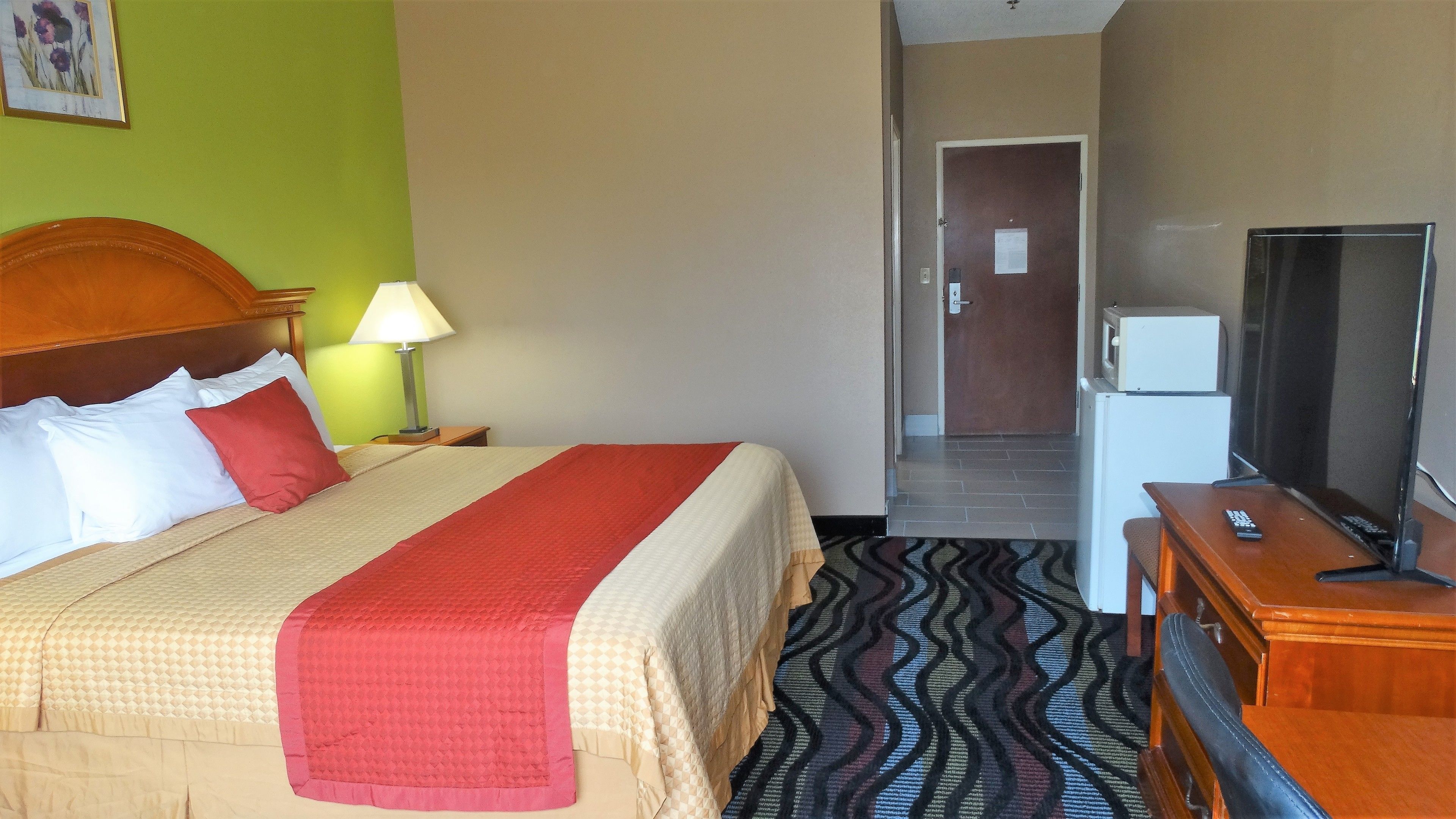 A hotel room with a bed, a nightstand, a lamp, a dresser, a television, and a door leading to another room.