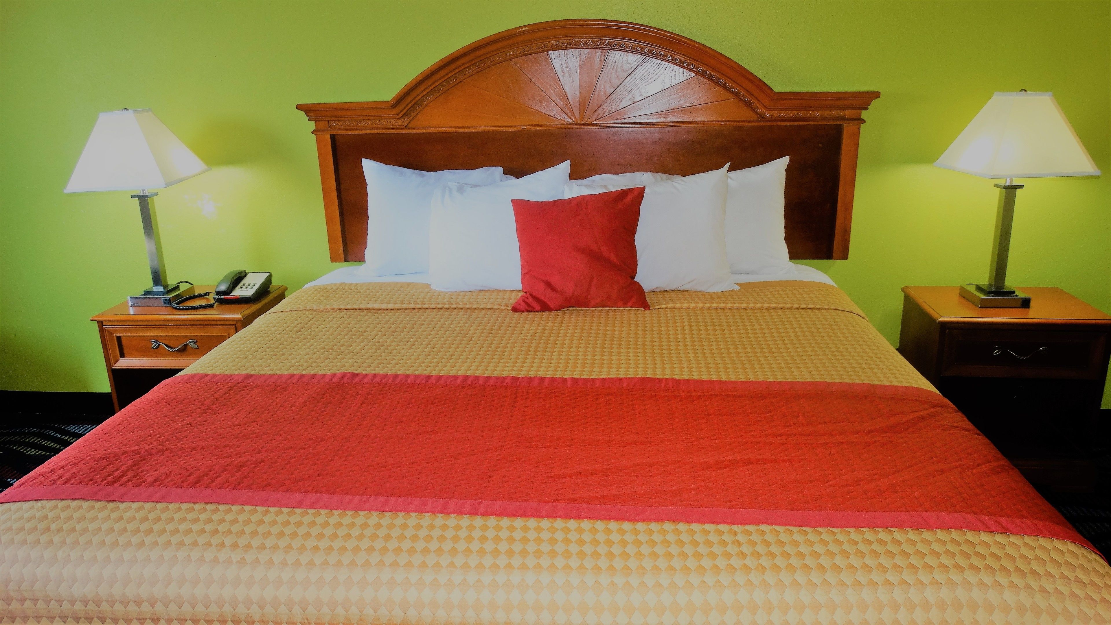 A neatly made bed with a red pillow, two bedside tables with lamps, and a wooden headboard.