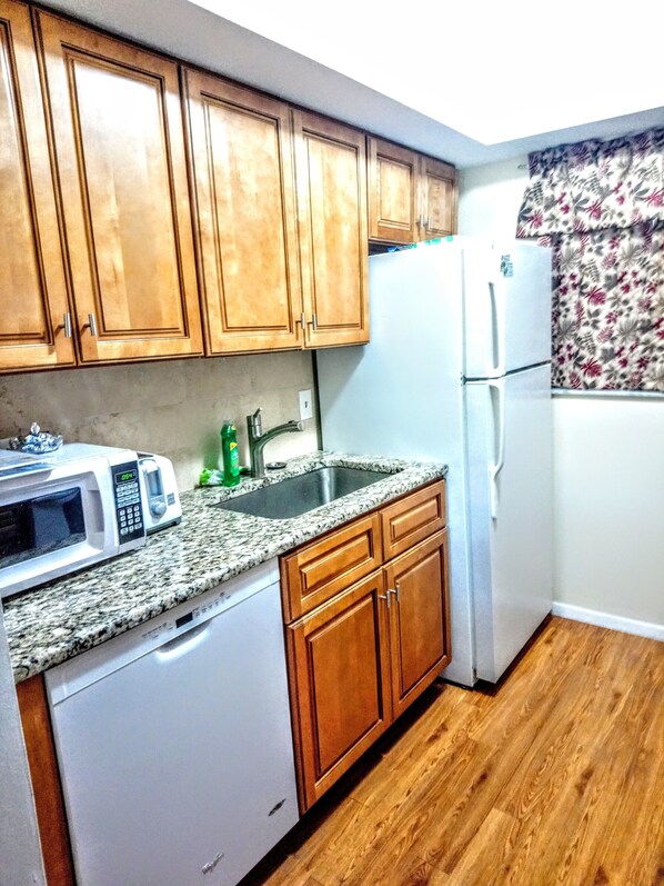 A kitchen with wooden cabinets, a granite countertop, a white dishwasher, a white refrigerator, and a stainless steel sink. - Tropical Dreams - Sarasota Condos Near Siesta Key (Sarasota)