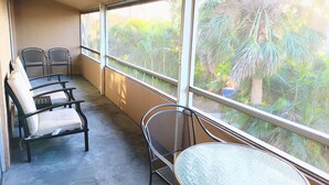 Un balcón con dos sillas, una mesa y vista a un jardín con palmeras.