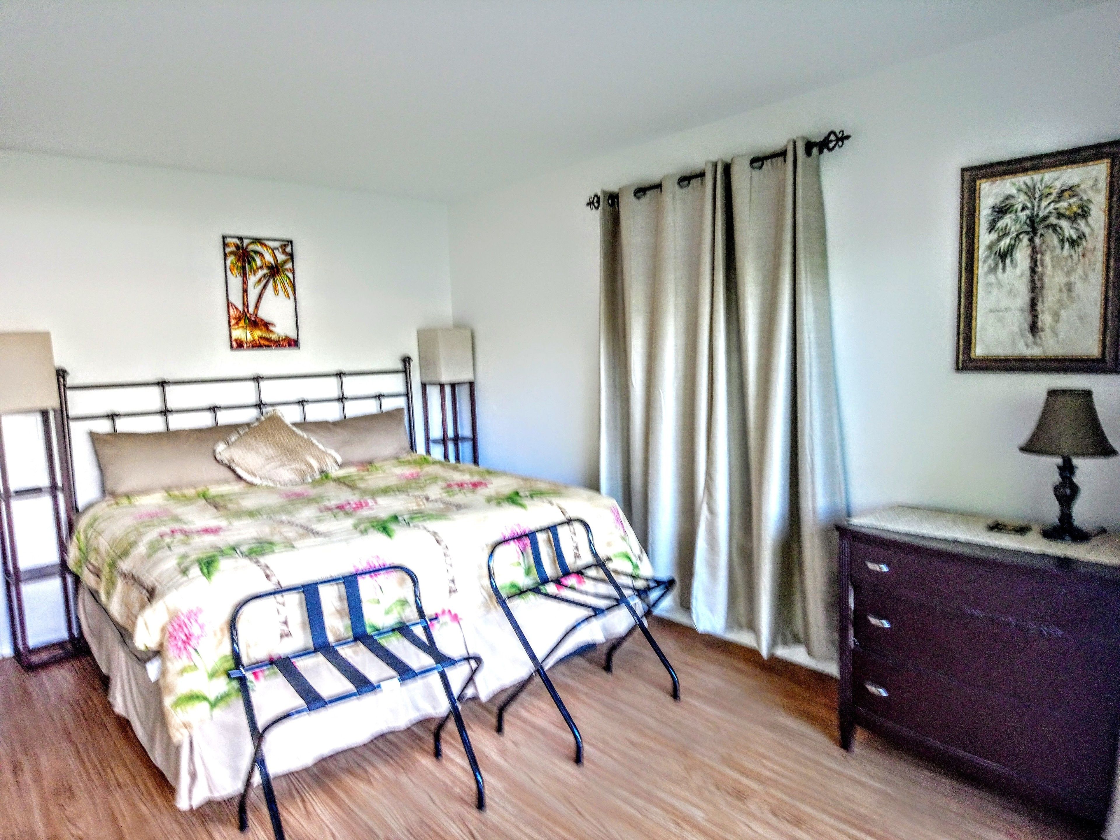 A bedroom with a bed, a nightstand, a dresser, and a window with curtains.
