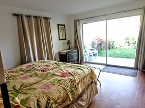 A bedroom with a bed, a dresser, a lamp, and a view of the outdoors through a sliding glass door.