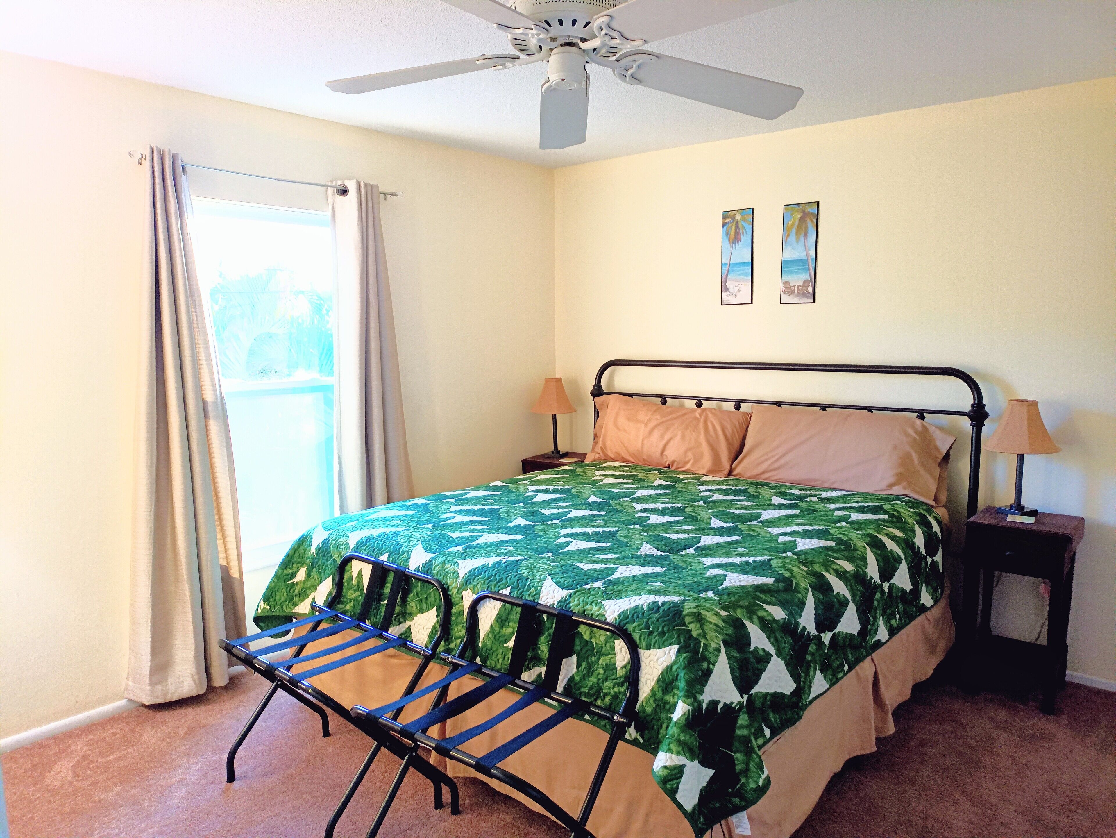 A bedroom with a bed, a ceiling fan, a window with curtains, and two wall-mounted pictures.