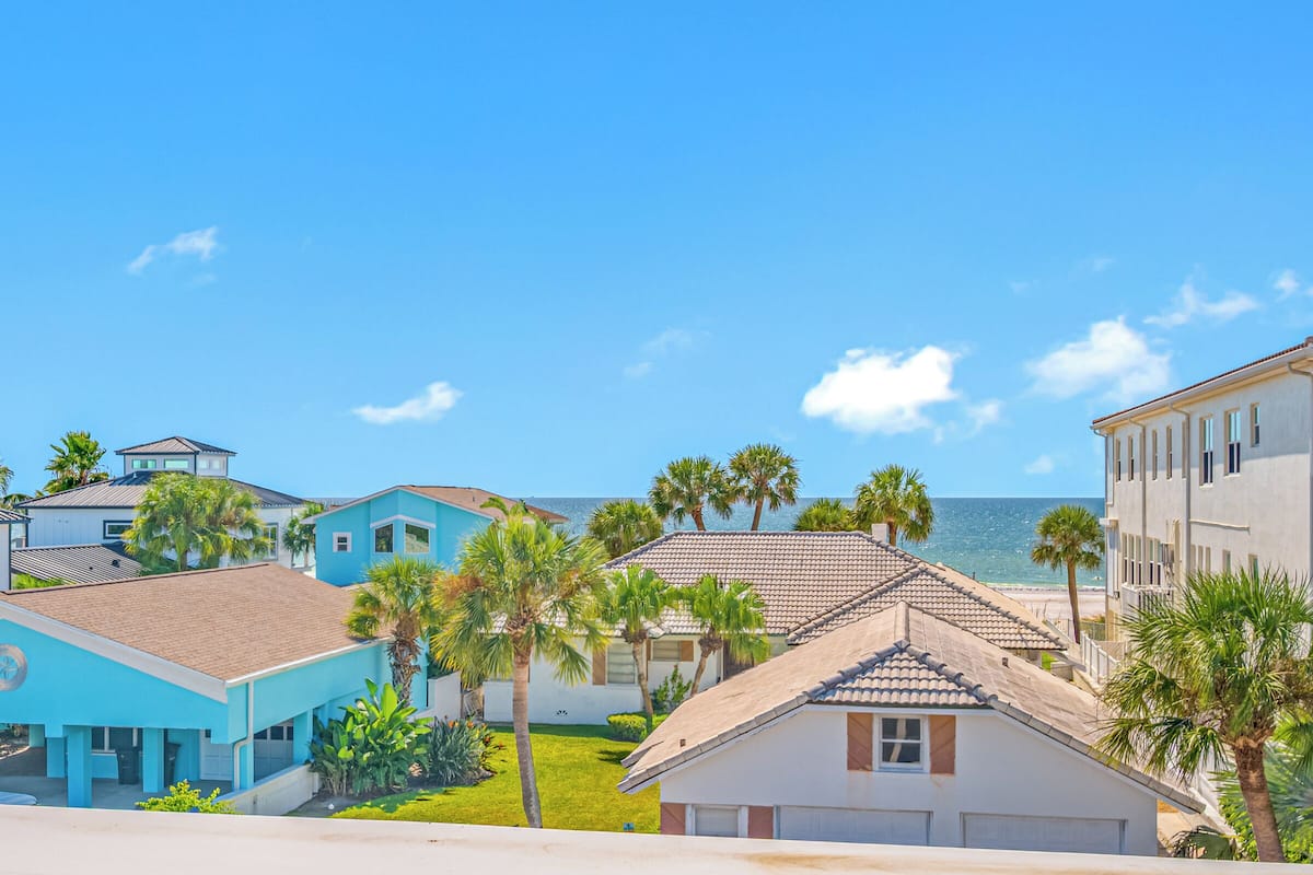 A coastal residential area with houses, palm trees, and a clear view of the ocean.