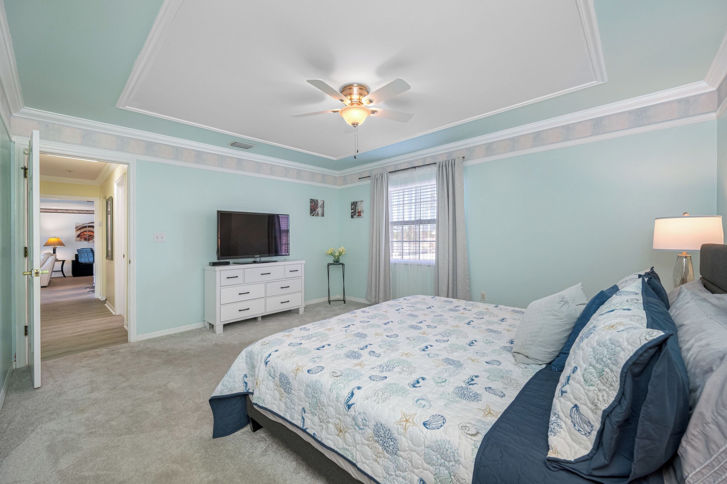 Un dormitorio con una cama, ventilador de techo, televisor y cómoda.