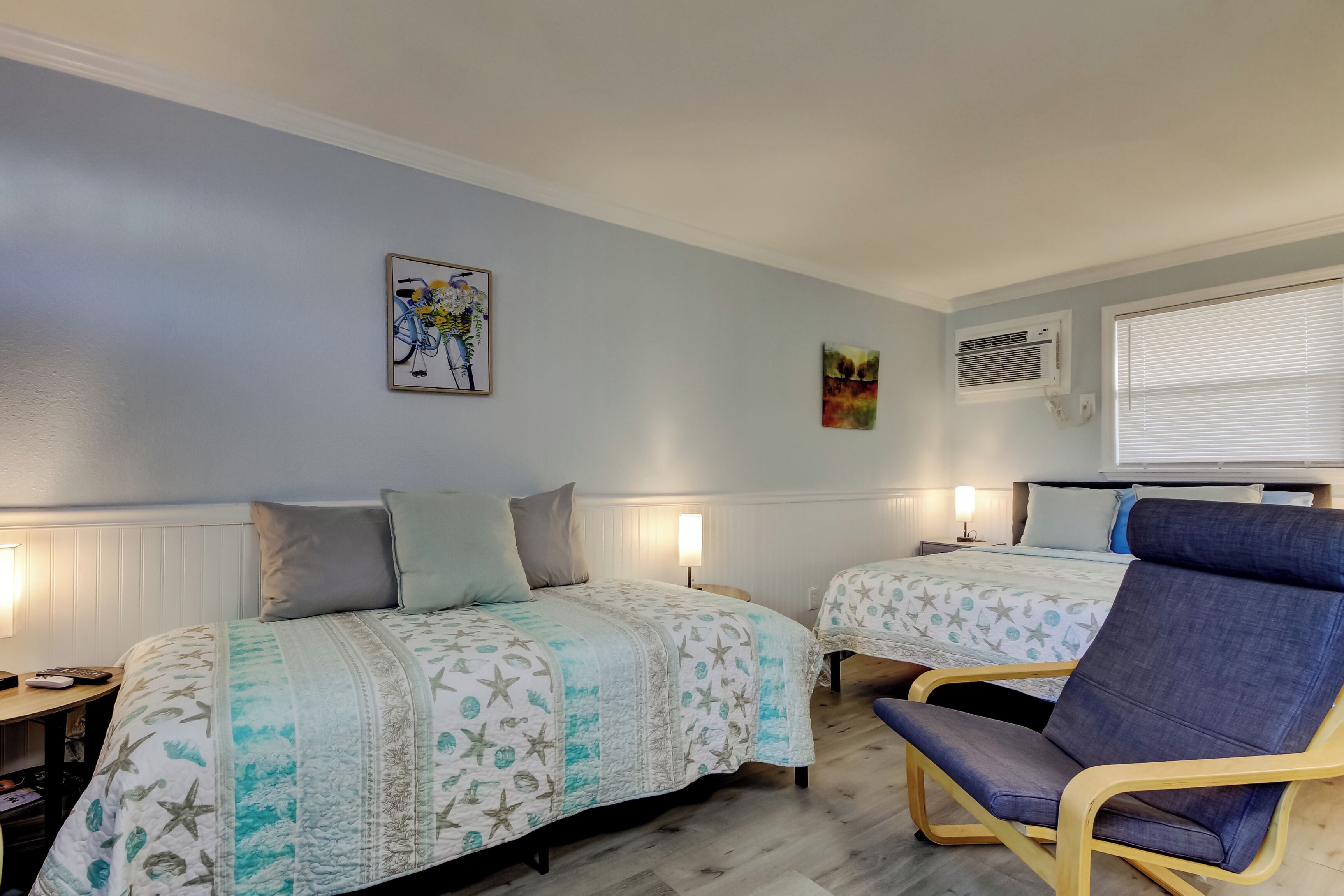 A bedroom with two beds, a chair, and artwork on the wall.
