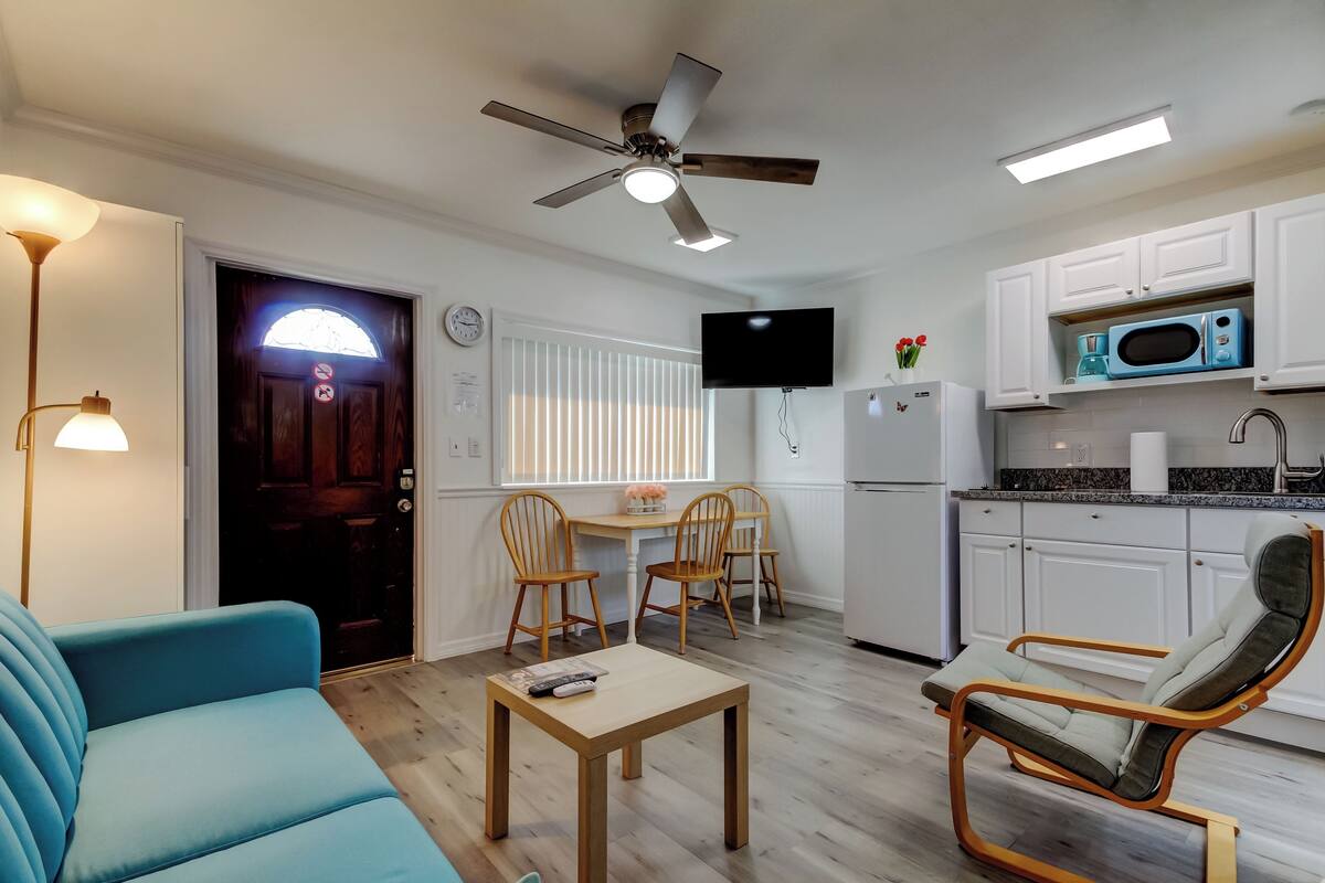 A compact living space with a kitchenette, a dining area with chairs, a sofa, and a ceiling fan.