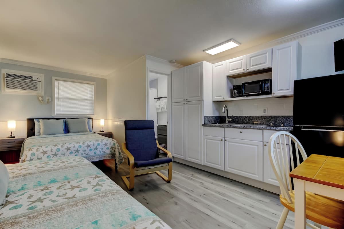 A compact hotel room with a bed, a chair, a small table, and a kitchenette.