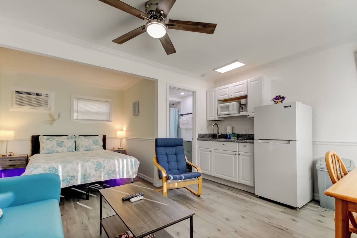 A bedroom with a bed, a blue armchair, a wooden table, and a ceiling fan.