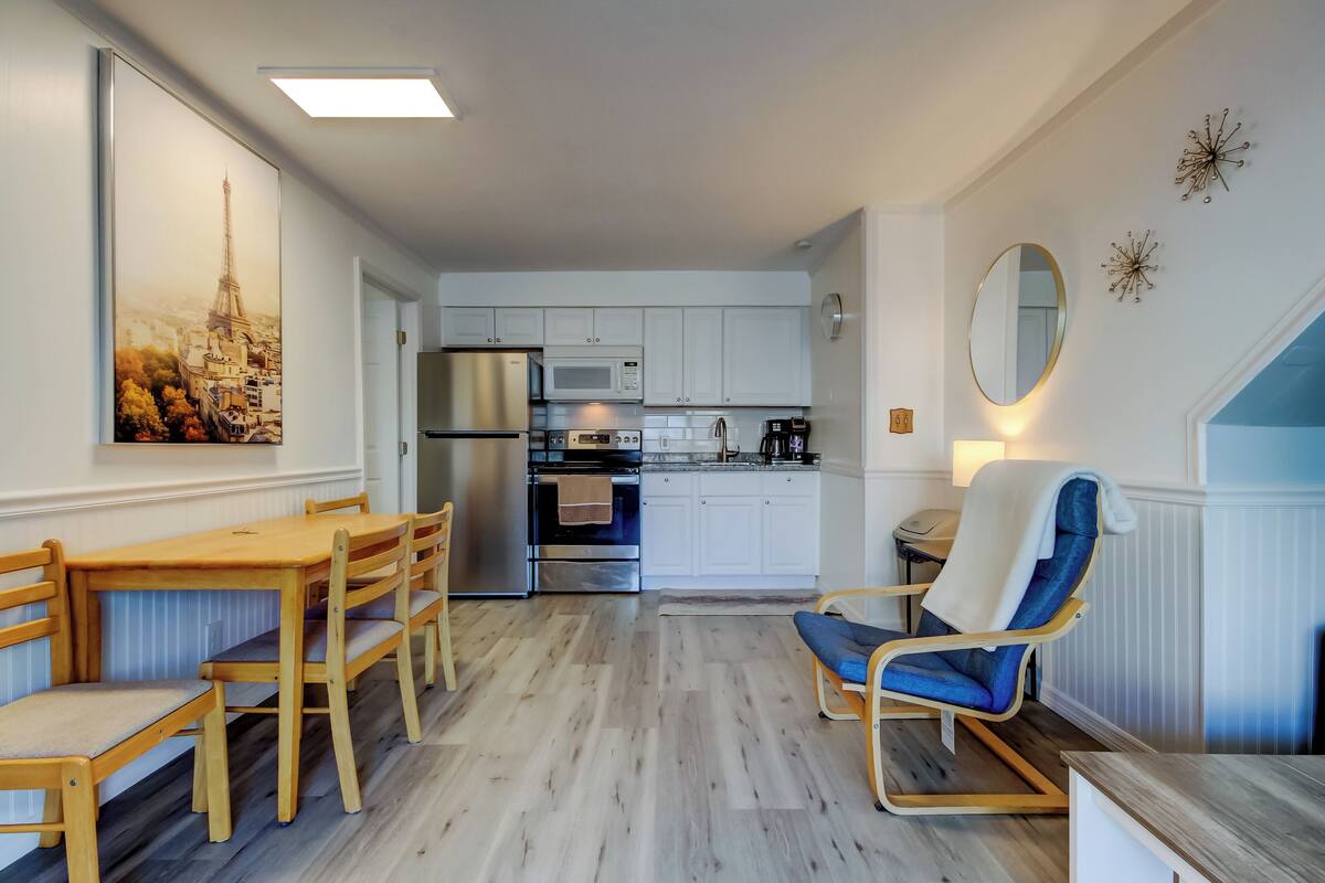 A modern kitchen with white cabinets, stainless steel appliances, and a dining area with wooden furniture.