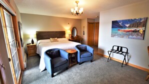Habitación de hotel con una cama grande, dos sillones, una mesita, un espejo, una lámpara y un cuadro de un lago.