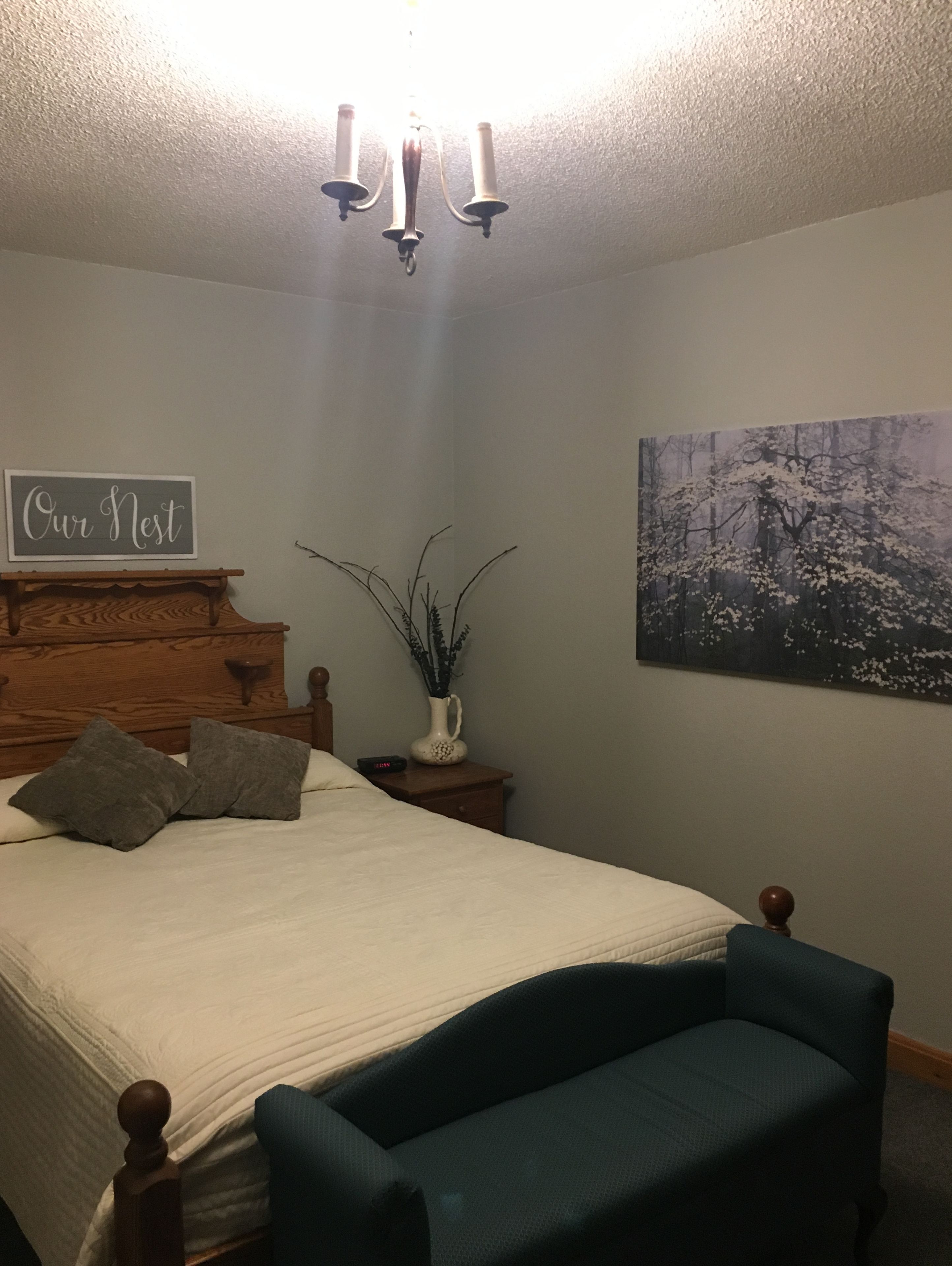 Un dormitorio con cama, mesitas de noche, una silla y un cuadro, además de un letrero en la pared.