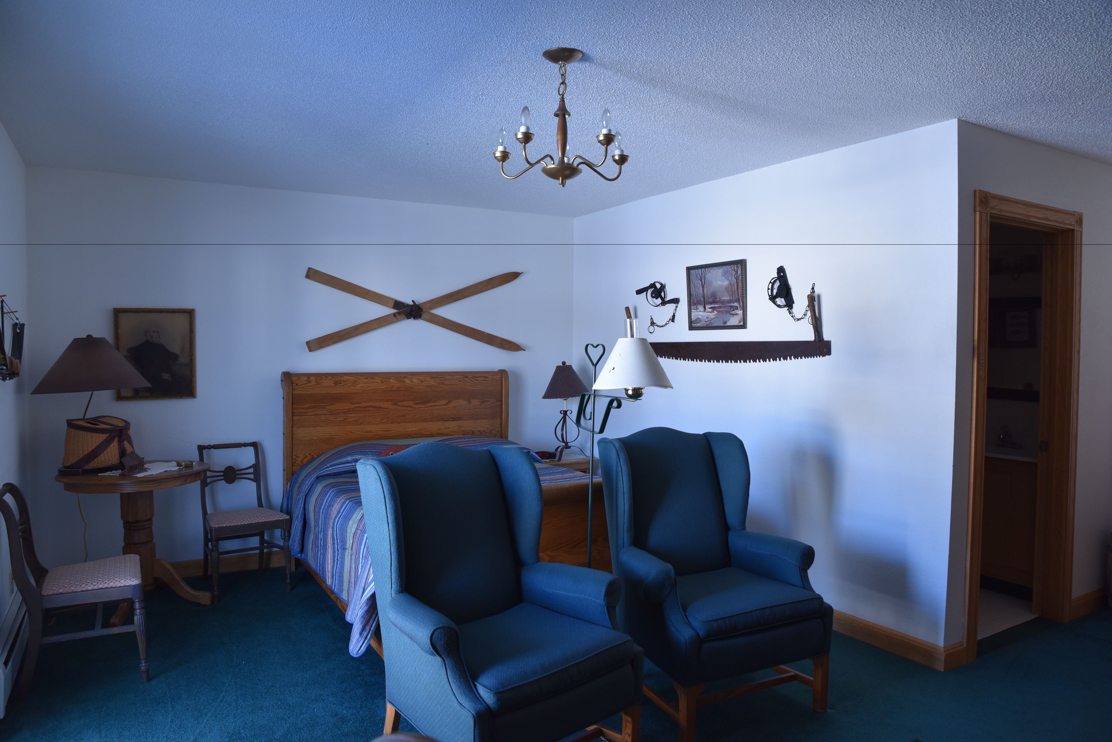A bedroom with a wooden headboard, two blue armchairs, a ceiling fan, a chandelier, and a bed with a striped blanket.