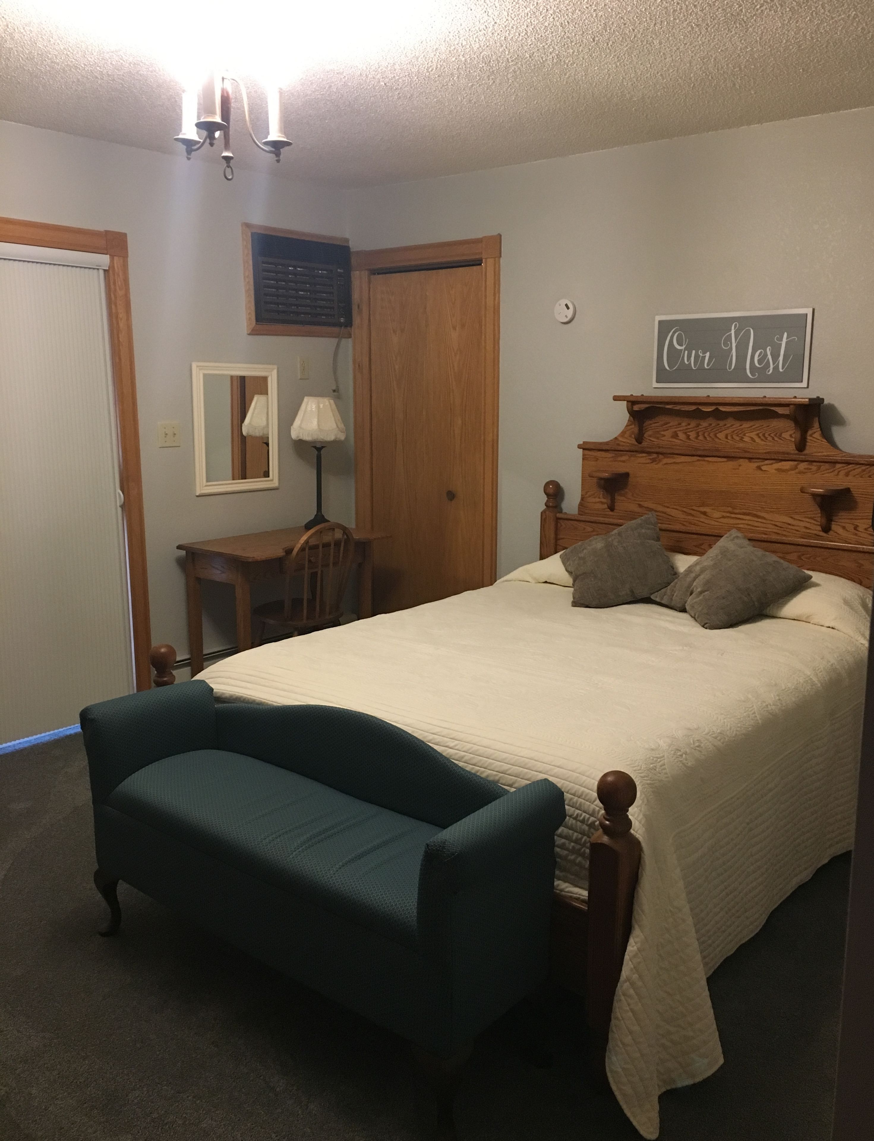 Un dormitorio con cama, una silla, una lámpara, un aparador de madera y un reloj de pared.
