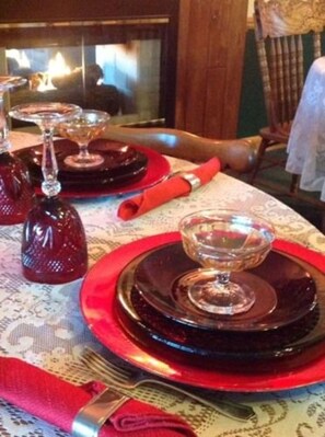 Una mesa dispuesta con platos rojos, copas de cristal transparentes y un mantel estampado.