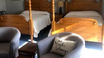 A bedroom with two wooden four-poster beds, a small table, and two armchairs.